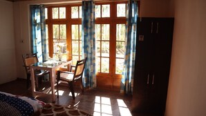 Um quarto com uma mesa e cadeiras de madeira, uma cama com colcha estampada e uma janela com cortinas azuis.