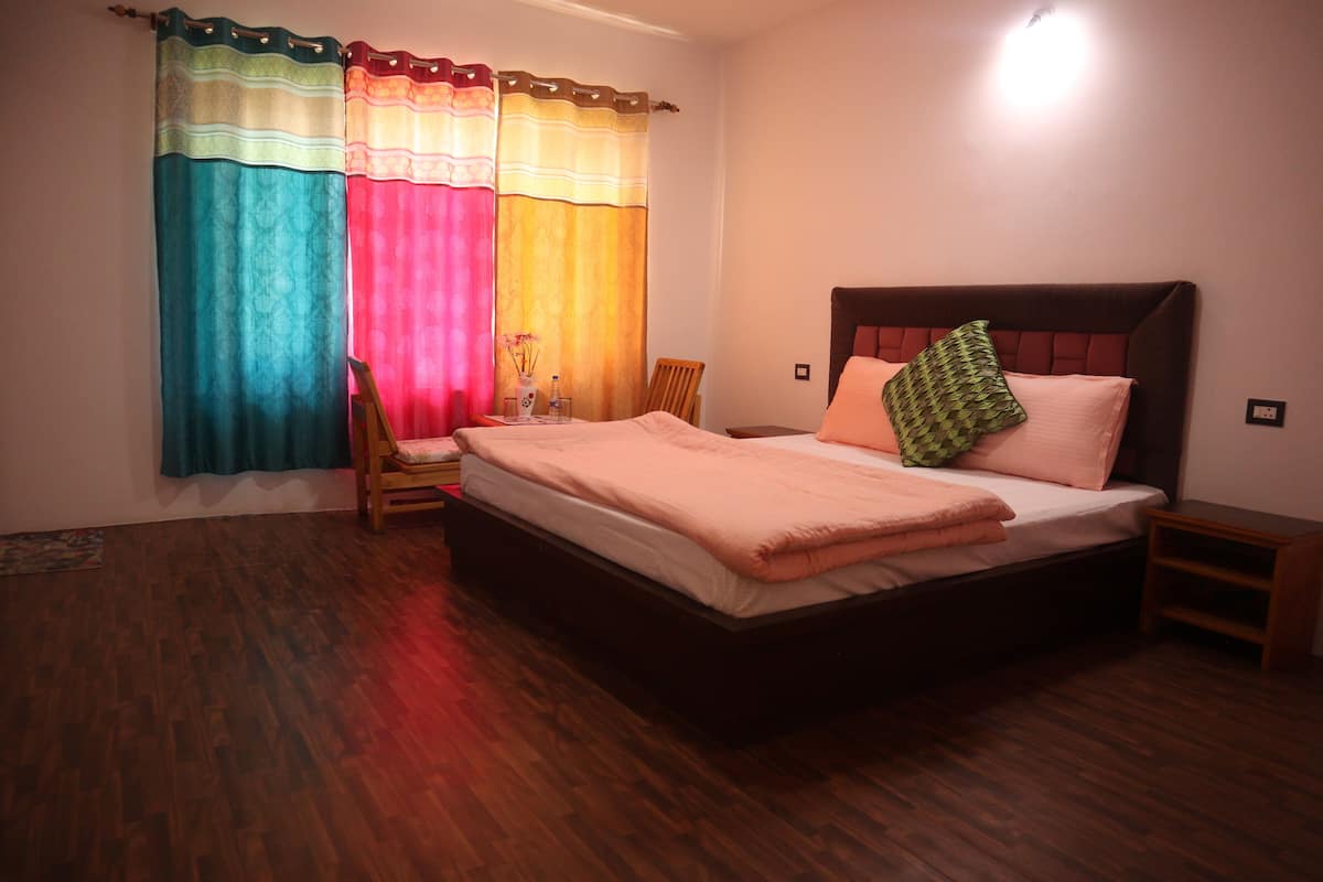 A bedroom with a wooden floor, a bed with a headboard, a chair, and a nightstand.