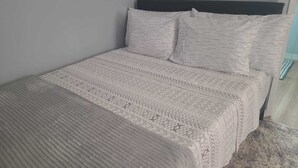 A bed with a patterned bedspread and pillows, a headboard, and a carpeted floor. - Sunburst Studio (Caicos Islands)