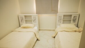 A small, clean room with two beds, a nightstand on each side, and a marble-patterned floor.