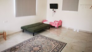 A room with a green sofa, a pink child's bed, a patterned rug, and a flat-screen TV mounted on the wall.