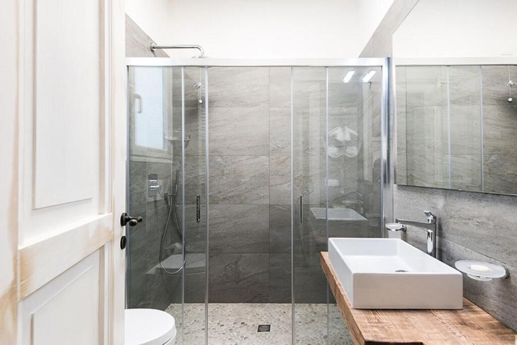 Un baño moderno con ducha acristalada, lavamanos blanco y tocador de madera.