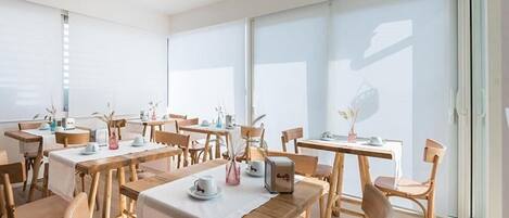 A modern dining area with wooden tables and chairs, large windows, and minimalistic decor.