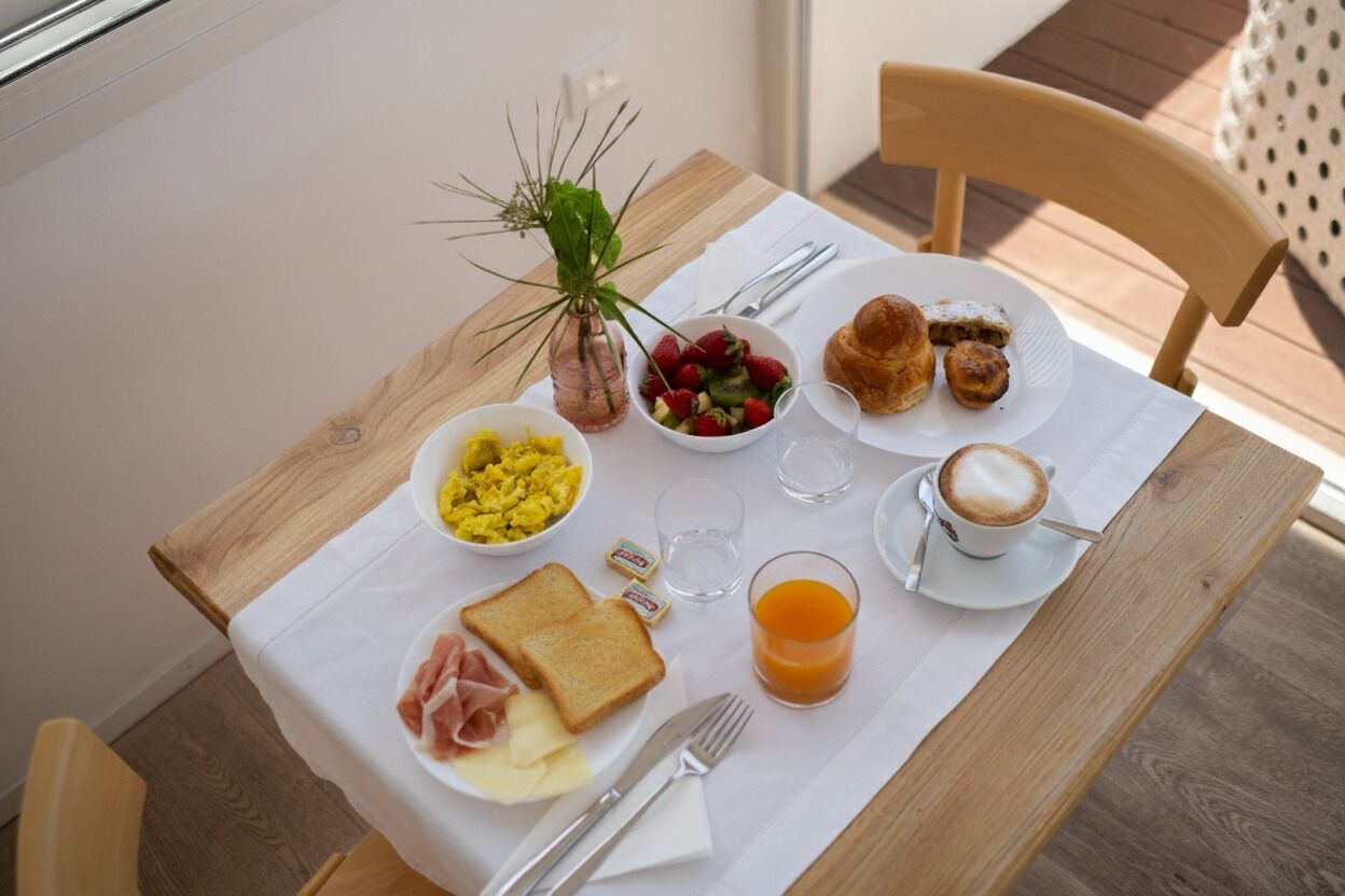 A breakfast table with toast, scrambled eggs, a bowl of fruit, croissants, and a cup of coffee.