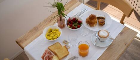 A breakfast table with toast, scrambled eggs, a bowl of fruit, croissants, and a cup of coffee.
