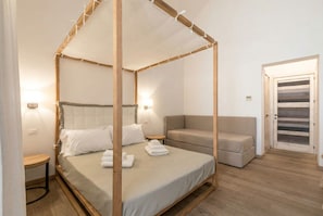 A four-poster bed with a canopy, a sofa, a small round table, and a door with a striped pattern. - B&B Il Palazzotto di Luca Luxury Suites (Lecce)