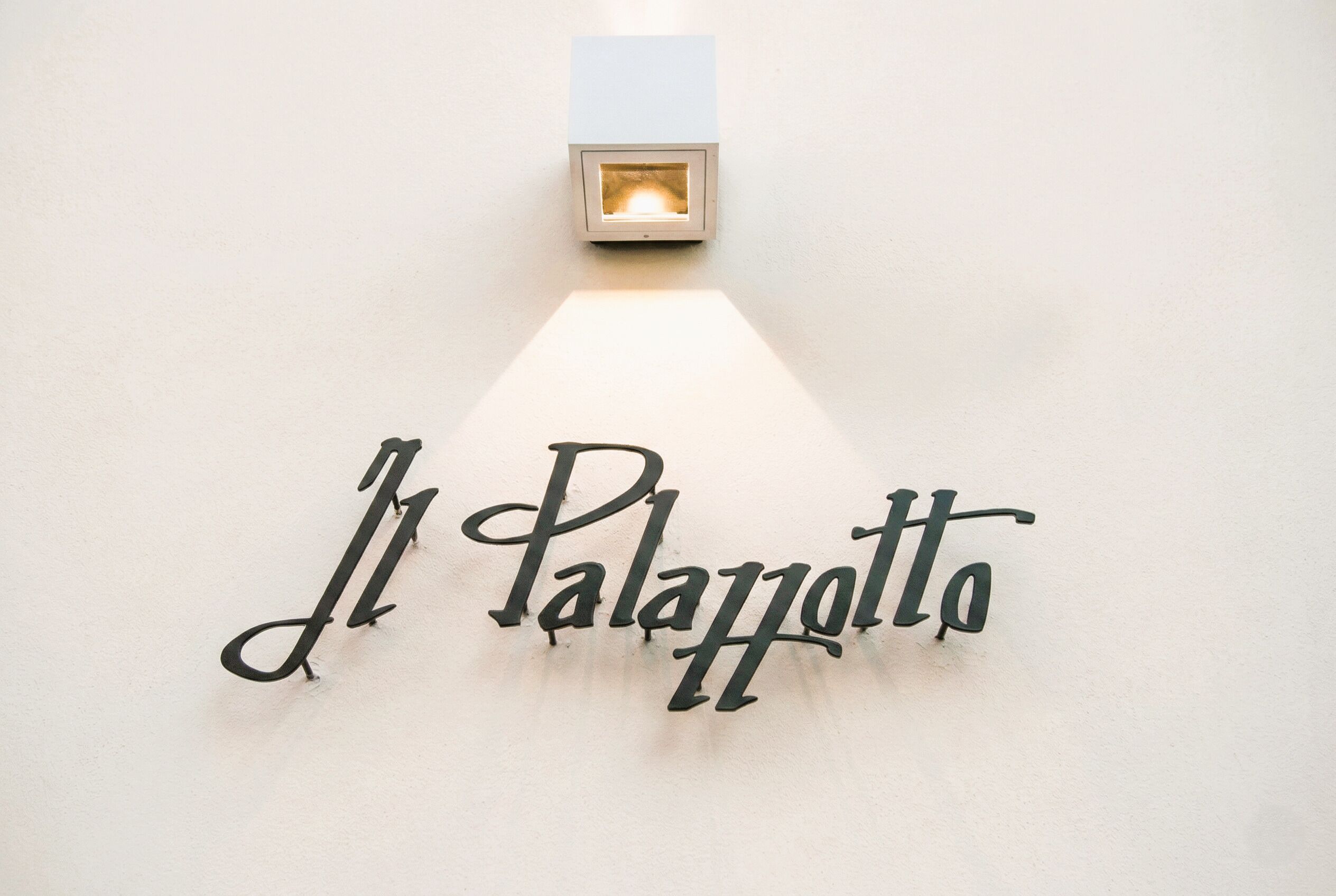 A wall-mounted sign with the name "Il Palazzetto" illuminated by a light fixture.