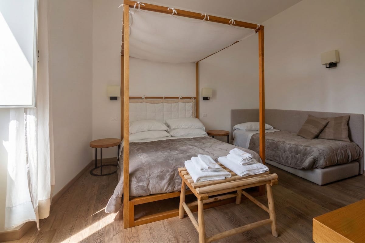 Una cama con dosel y cortinas, una mesita de noche con toallas, un sofá y una pequeña mesa redonda.