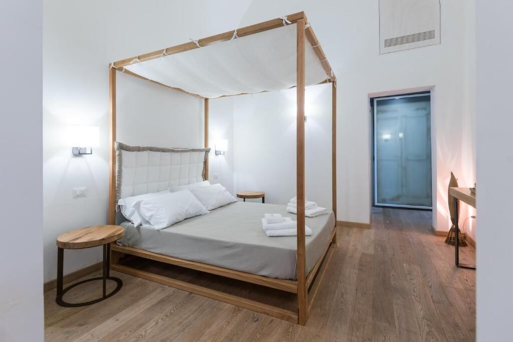 Un letto a baldacchino con struttura in legno e biancheria bianca, un piccolo tavolino rotondo accanto e una porta sullo sfondo.