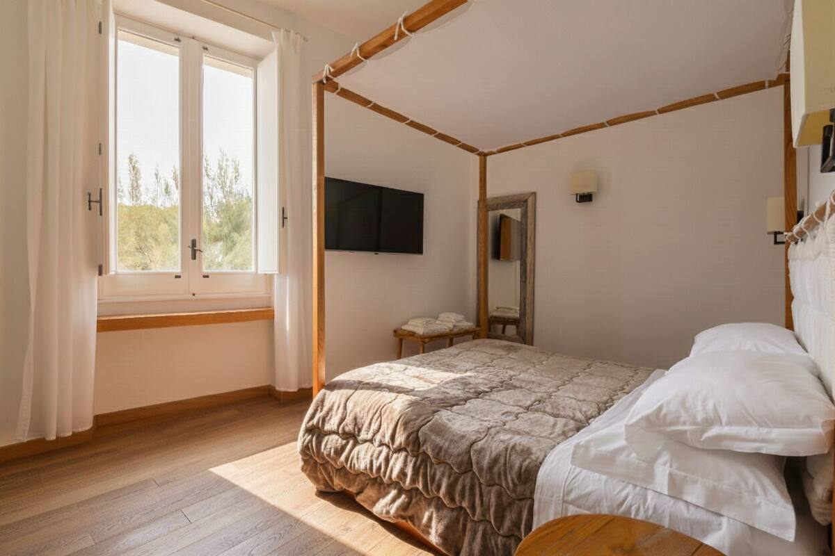 Una cama con dosel, un edredón, una mesita de noche, un espejo y una ventana con cortinas.