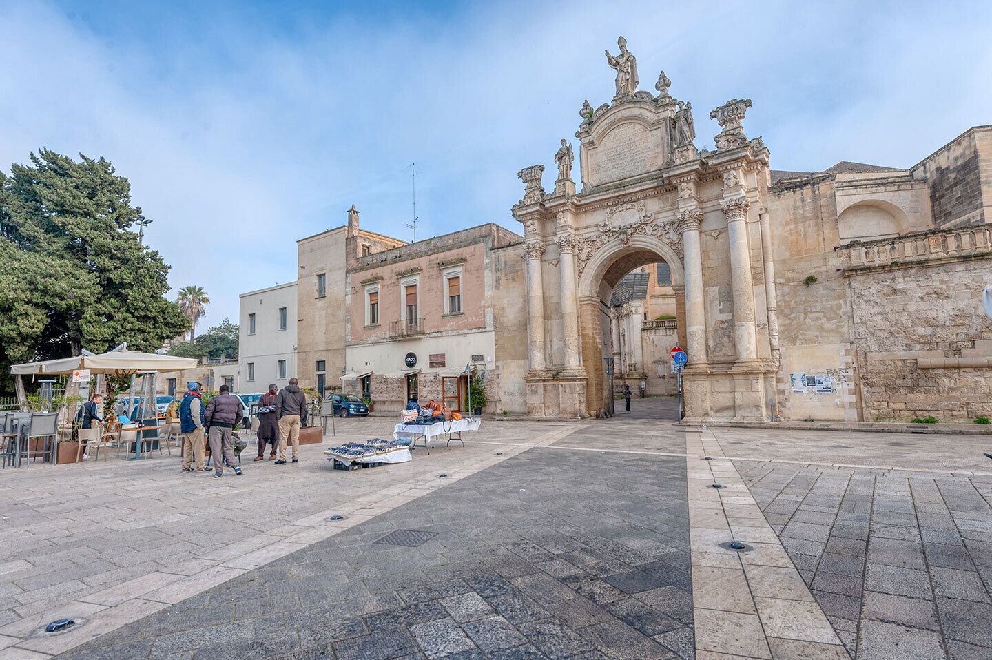 A historic stone archway with intricate carvings and statues, leading to a building with classical architecture.