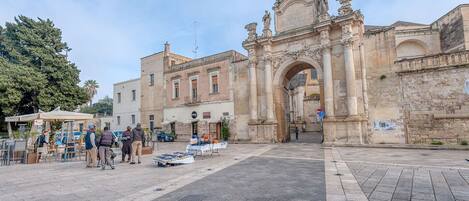 A historic stone archway with intricate carvings and statues, leading to a building with classical architecture.