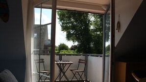 A balcony with a table and two chairs, a view of trees and buildings, and a glass door.