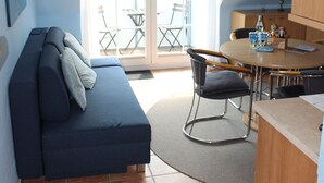 A compact living space with a sofa, a dining table with chairs, and a sliding glass door leading to an outdoor patio.