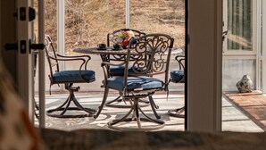 An open door leading to a patio with a table and chairs, a decorative lamp, and a view of a wooded area.