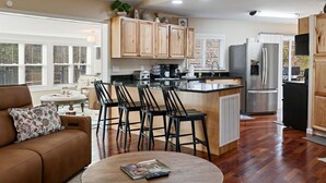 A modern kitchen with wooden cabinets, a stainless steel refrigerator, and a bar area with stools.