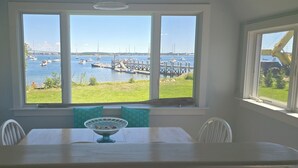Ein Essbereich mit Tisch und Stühlen, ein Fenster mit Blick auf eine Marina und Boote, und ein klarer Himmel.