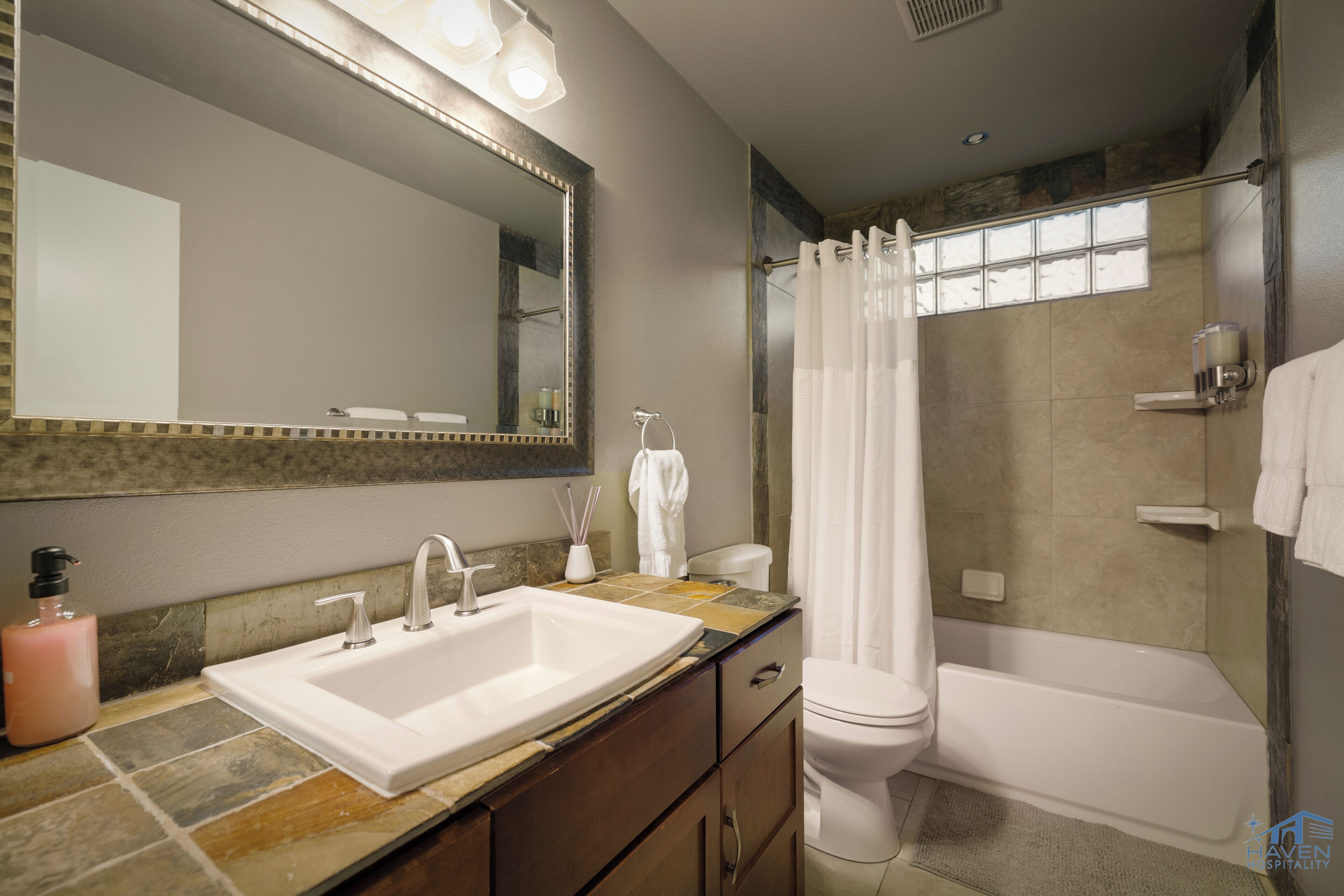 A bathroom with a sink, mirror, shower, and toilet.