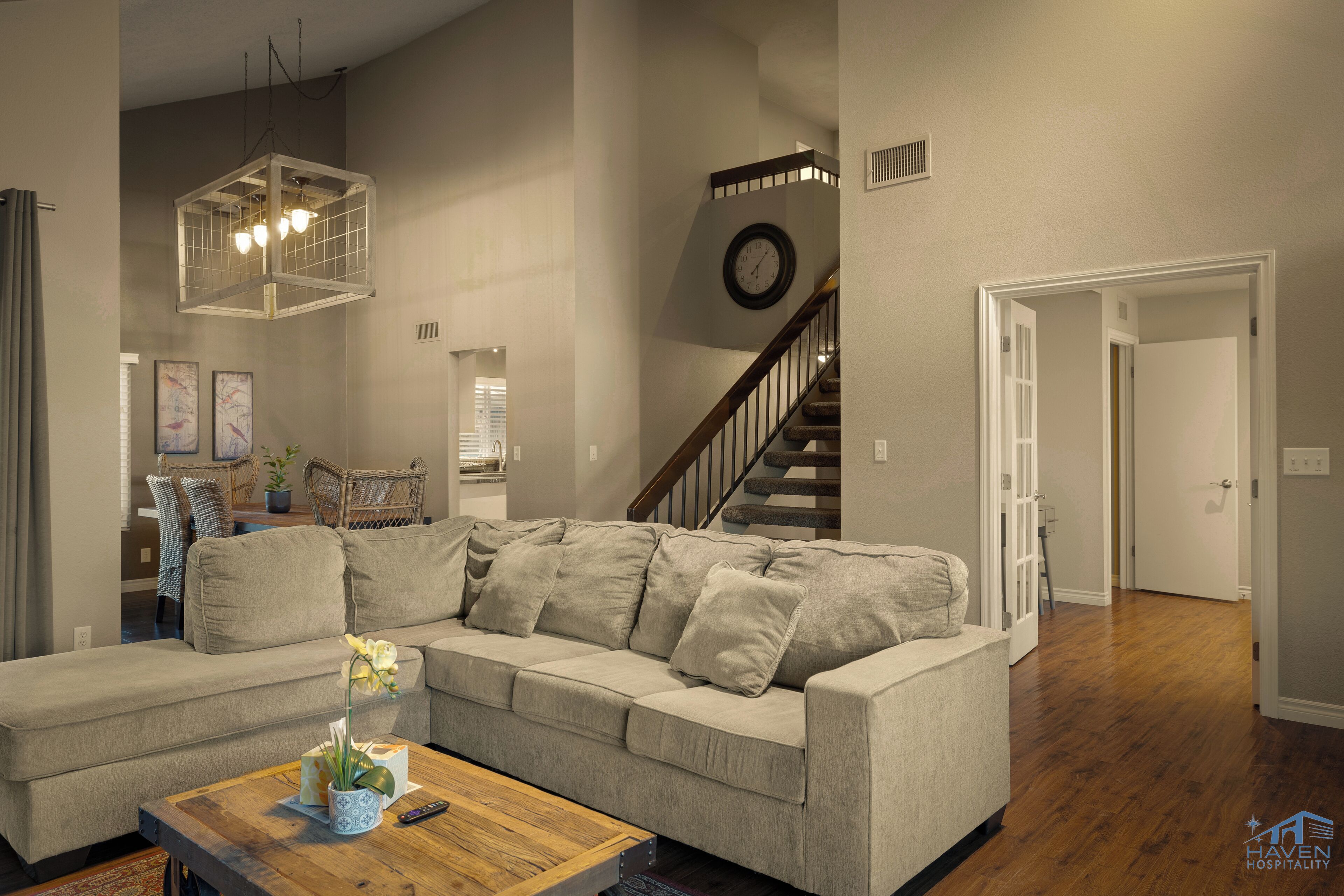 A spacious living room with a large beige sofa, a wooden coffee table, and a hanging light fixture.