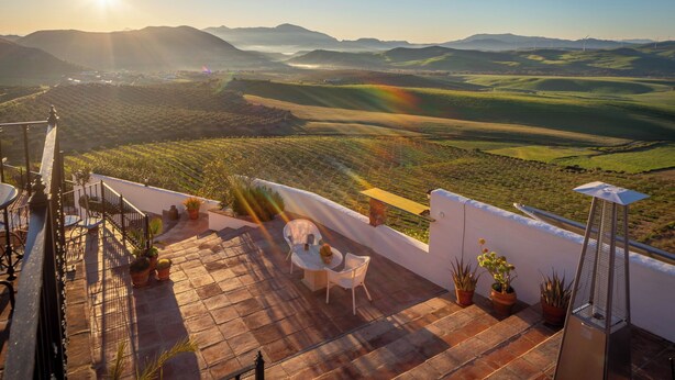 A terrace with a table and chairs, potted plants, and a view of rolling hills and wind turbines. - Boutique B&B Casa La Calera 15+/ Caminito del Rey-15 min/Ronda-25 min/Town-5 min (Teba)