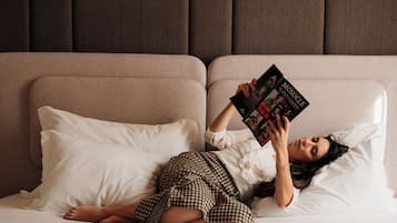 A person lying on a bed with a book, in a room with a headboard and pillows.