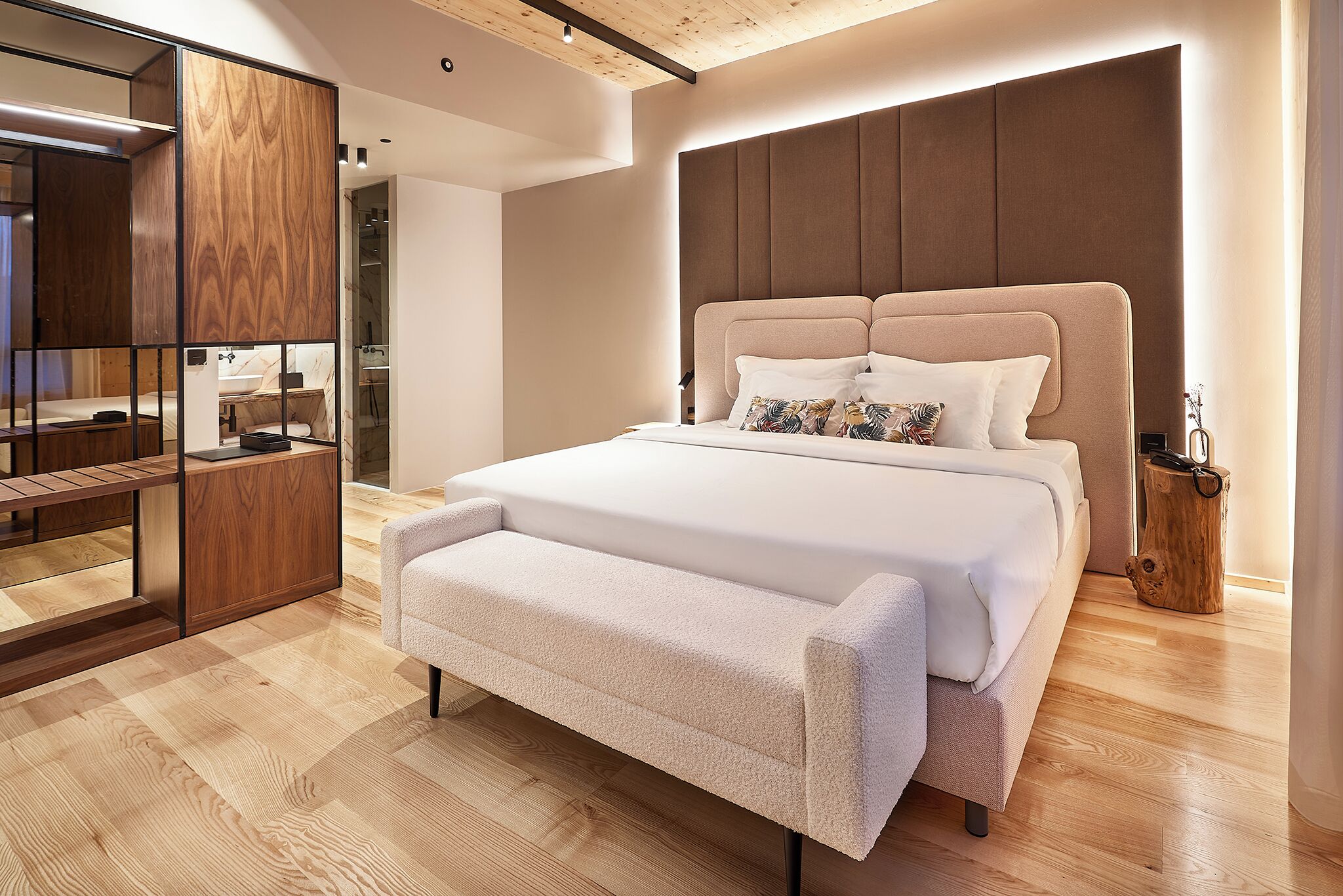 Een moderne slaapkamer met een groot bed, een houten garderobe en een bankje.