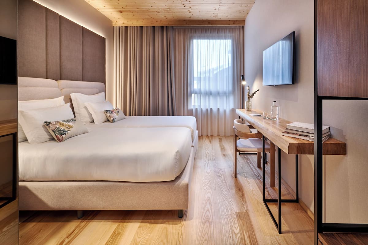 A modern hotel room with a large bed, a desk, and a TV mounted on the wall.