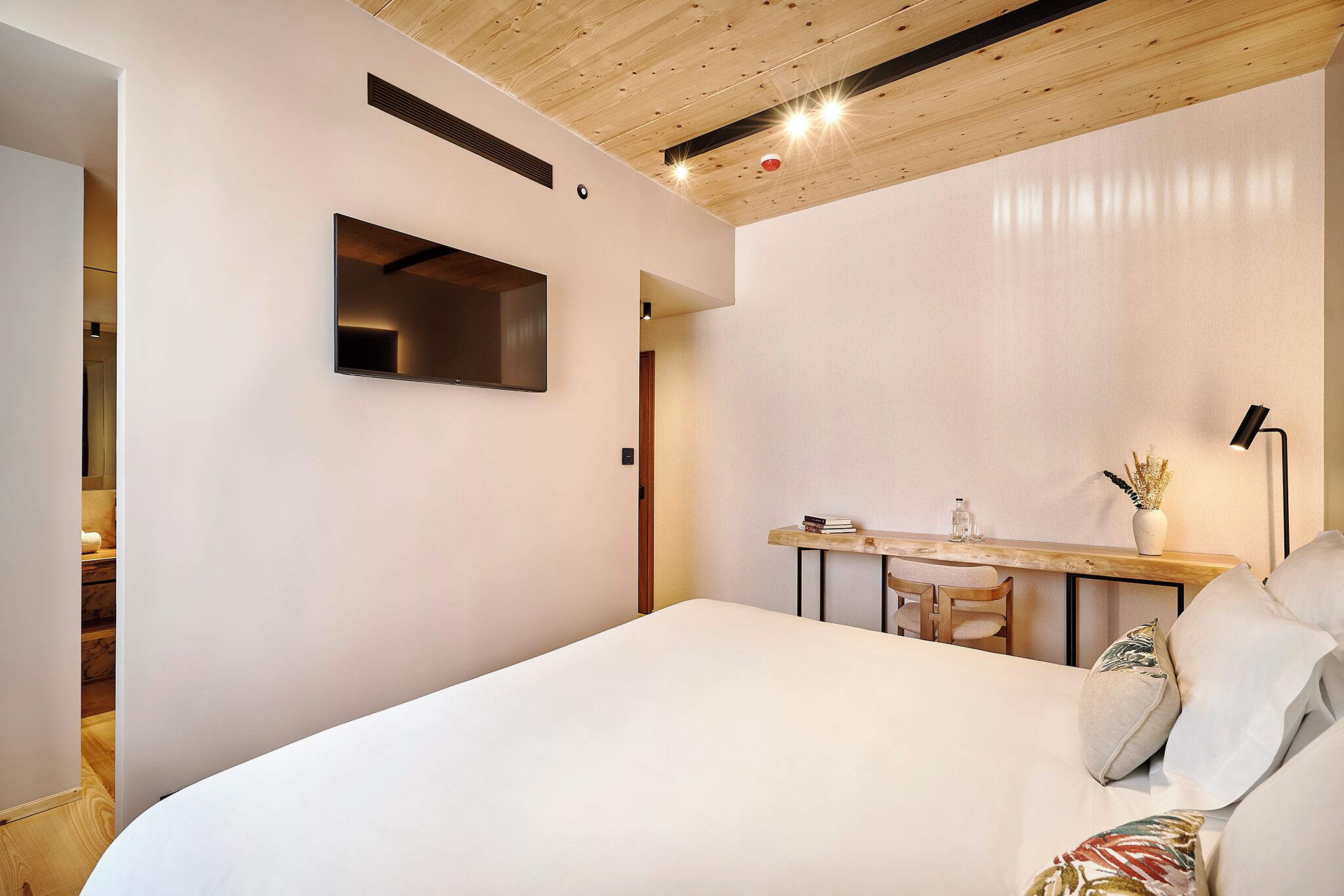 A modern bedroom with a large bed, a desk with a chair, and a TV mounted on the wall.