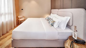A neatly made bed with white linens, a wooden nightstand with a phone and a small vase, and a wooden chair in a modern bedroom with wooden flooring and a wooden headboard.
