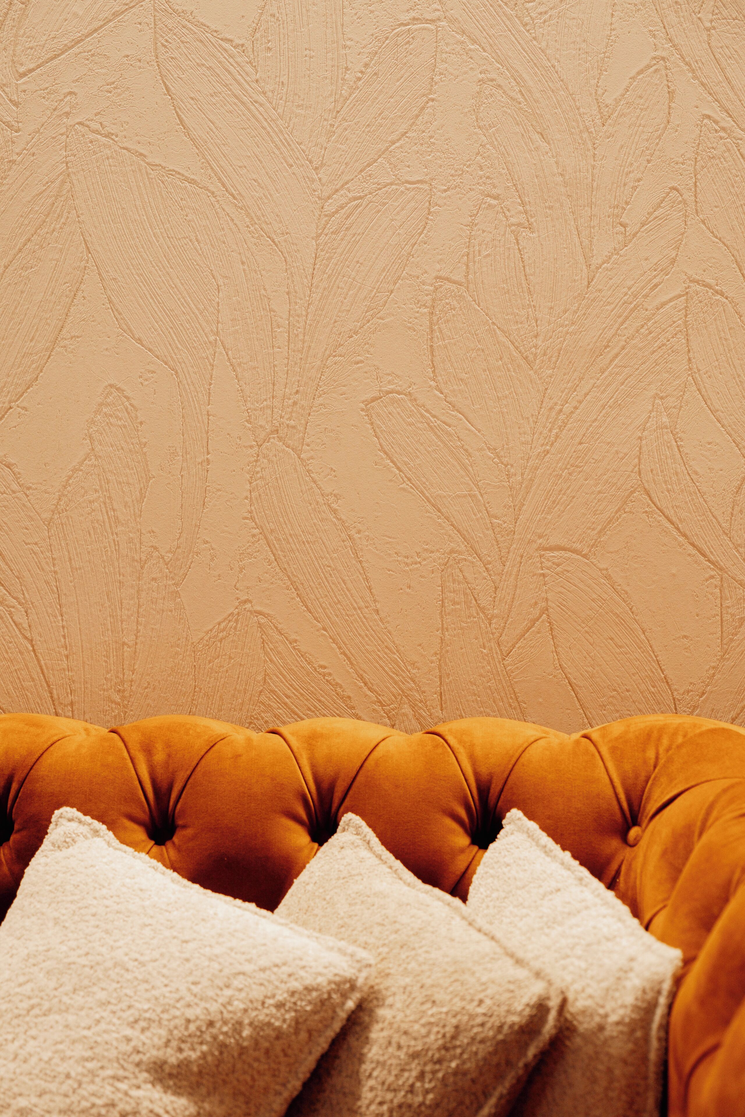 A tufted orange sofa with a textured beige wall in the background.