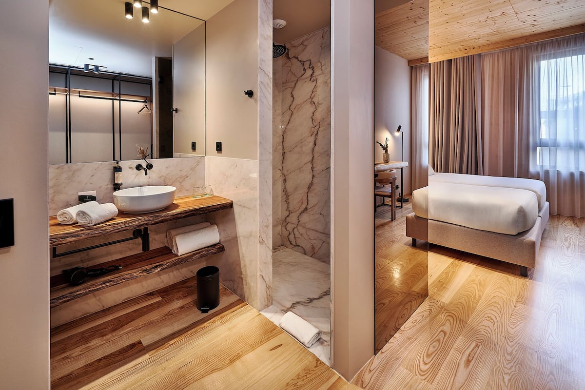 A modern bathroom with a marble sink, wooden vanity, and a shower with a marble wall.