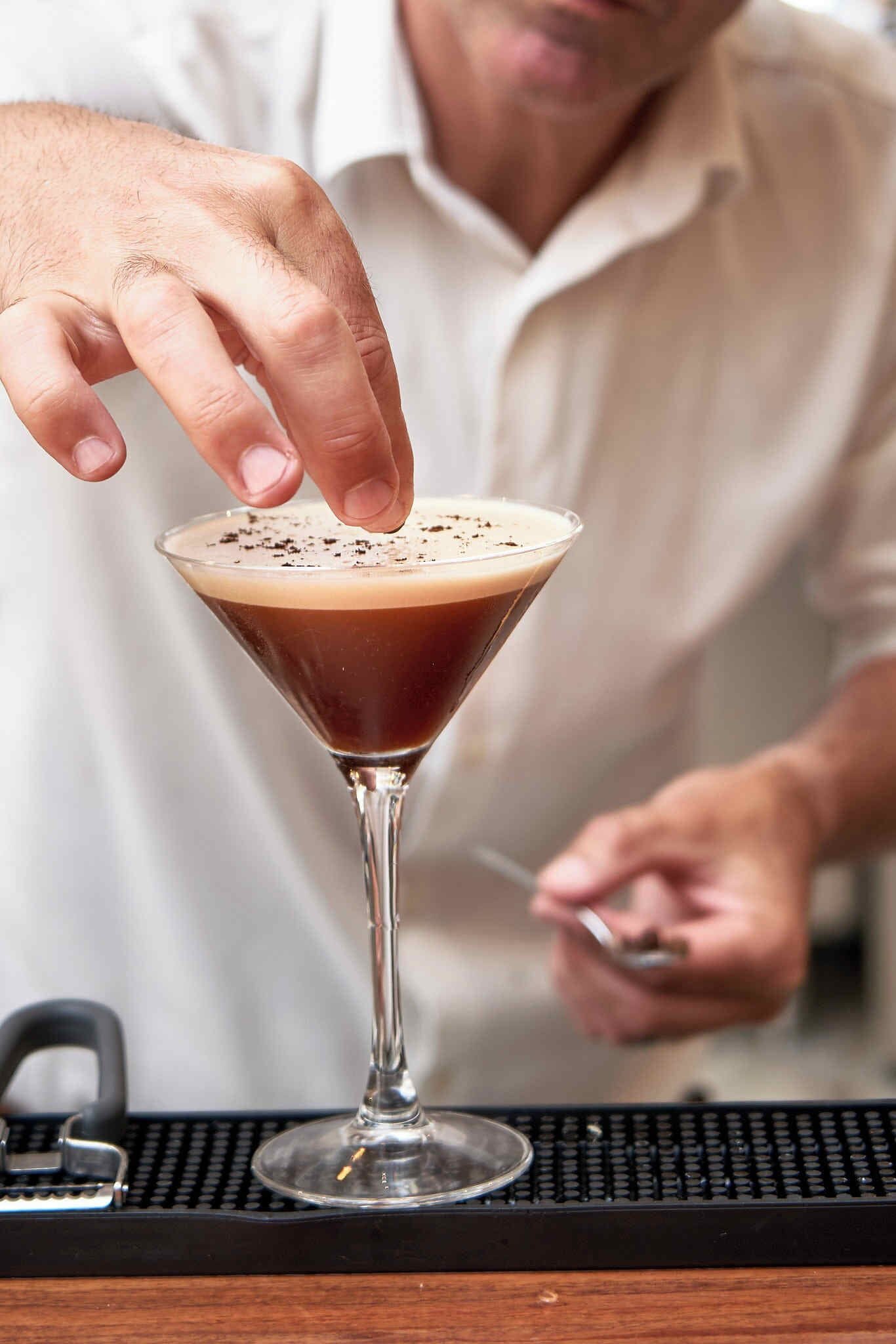 Una persona vertiendo un líquido oscuro en una copa de martini con una capa espesa y espumosa.