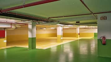 An indoor parking garage with green and yellow painted floors, red pipes on the ceiling, and a fire extinguisher on the wall.