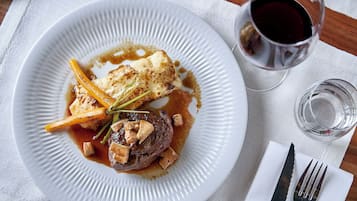 A plate of food with a fork and knife on a napkin, a glass of red wine, and a small glass of water.