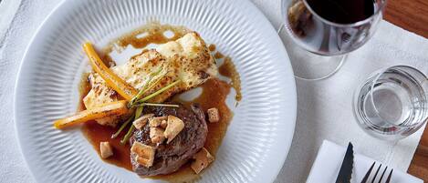 A plate of food with a fork and knife on a napkin, a glass of red wine, and a small glass of water.