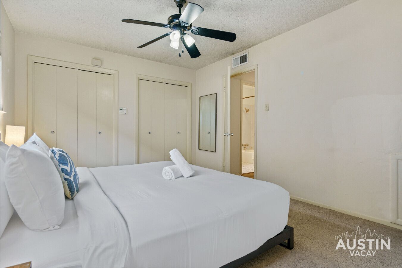 Una camera d'albergo con un letto, una ventola a soffitto e una porta che conduce al bagno.