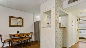 Un coin repas avec une table et des chaises en bois, un réfrigérateur et un miroir au mur.
