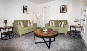 A living room with two green sofas, a round coffee table, and two side tables. - Beach House - 2 Bedrooms. Close to Beach & NC500 (Thurso)