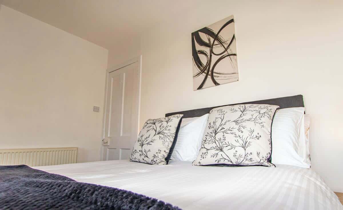 A bedroom with a bed, a radiator, a door, and a wall-mounted abstract art piece.