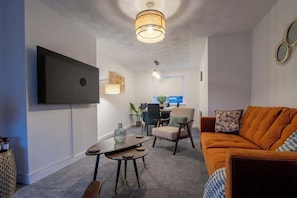 Un salon comprenant un canapé, une table basse, un téléviseur fixé au mur et un coin repas avec des chaises et une table.