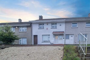 A row of two-story residential buildings with a gravel driveway and a small grassy area. - 3BR Near Glasgow | Free Parking | Ideal for Work (East Kilbride)