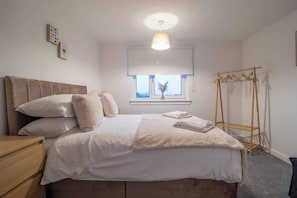 Une chambre à coucher avec un lit, une table de chevet, une fenêtre et un étendoir en bois.