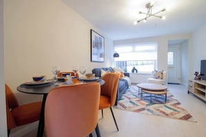 Un salon moderne comprenant un canapé, une table basse et un coin repas avec des chaises et une table dressée pour le repas.