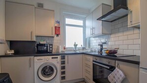 A compact kitchen with a washing machine, oven, microwave, and a window providing natural light.