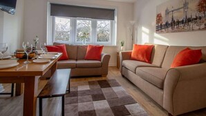 A living room with a sofa, a dining table set for four, and a window with a view of trees.