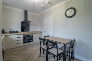 A modern kitchen with a built-in oven, a gas stove, and a stainless steel range hood. There is a wooden dining table with four chairs.