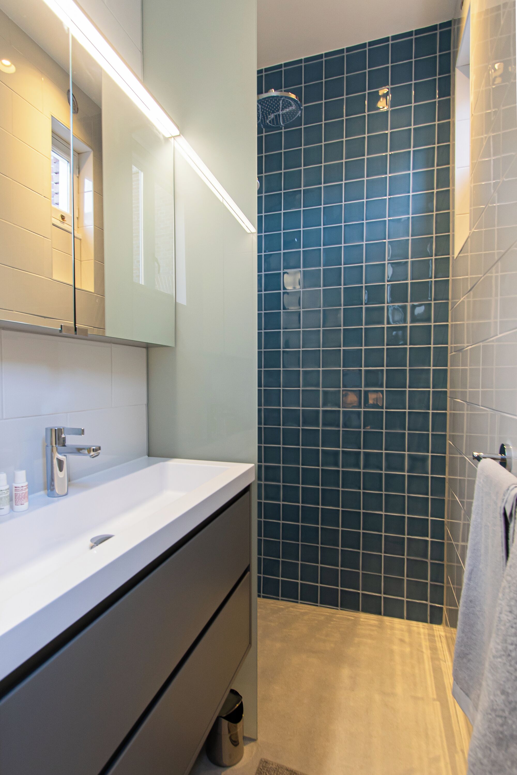 A modern bathroom with a white sink, mirror, and dark blue tiled shower wall.