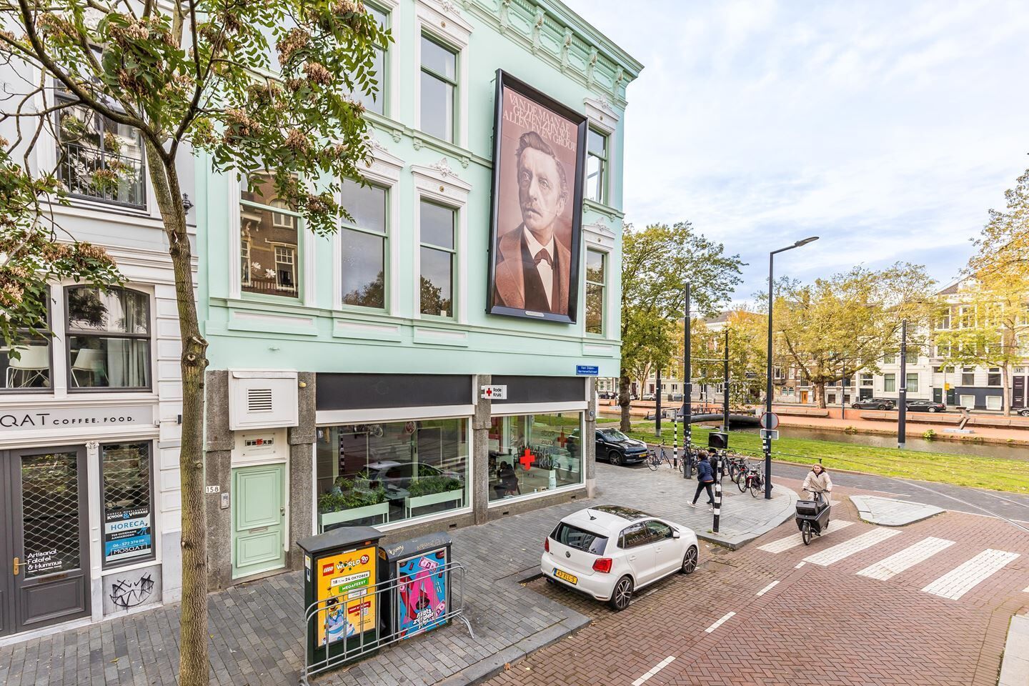 A street view of a building with a large poster, a café, and a parked car.