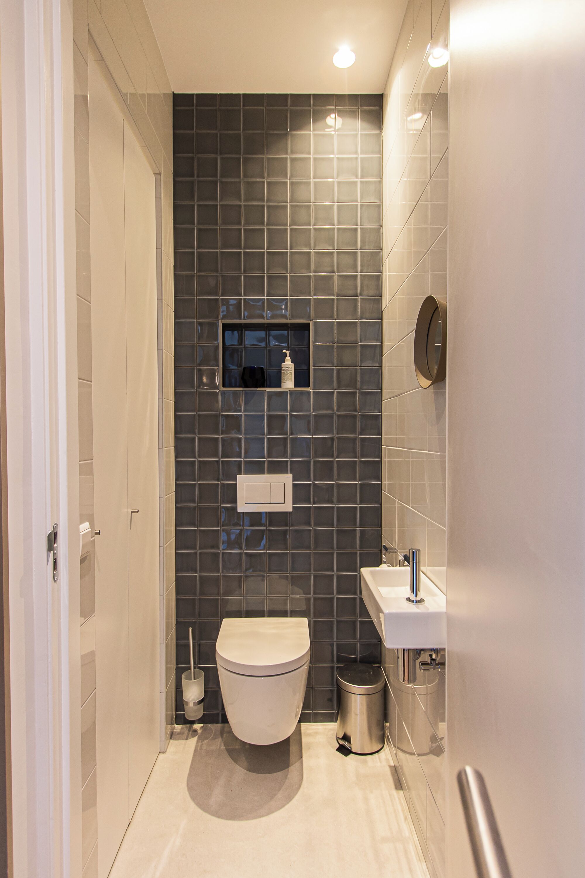 A modern bathroom with a toilet, sink, and storage shelves.