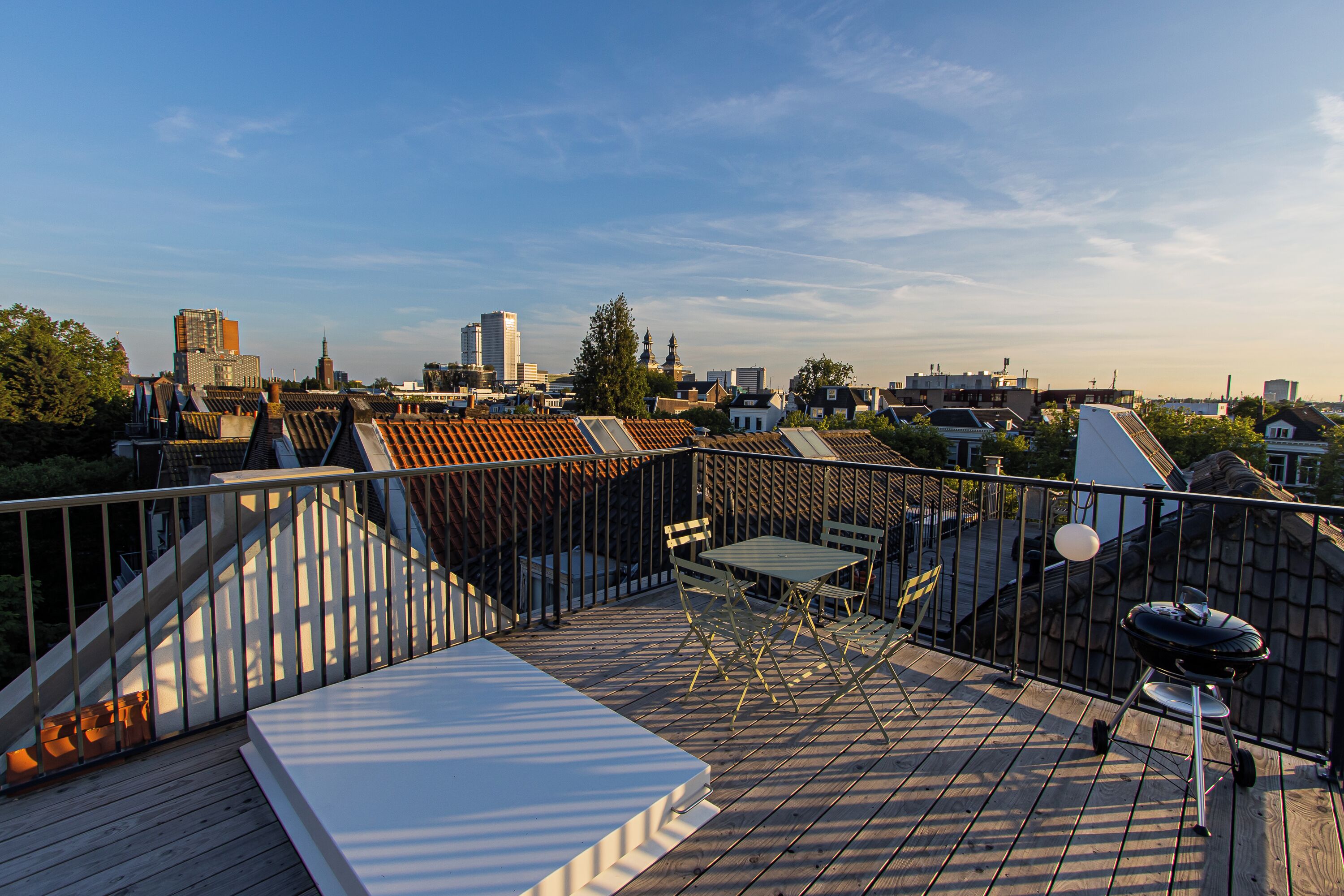 A rooftop terrace with a view of the city skyline, featuring a grill and outdoor seating.